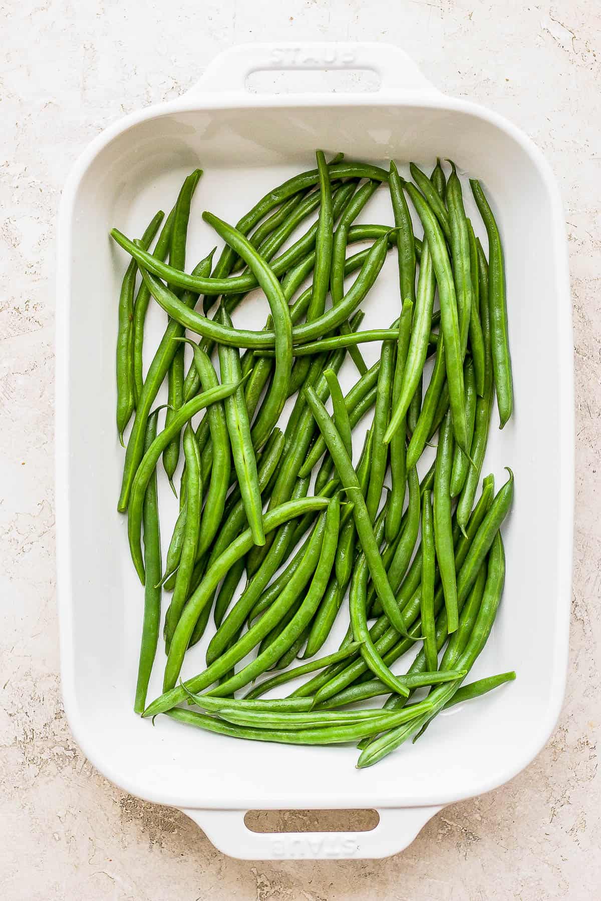 Blanched green beans spread out on the bottom of a casserole dish. 