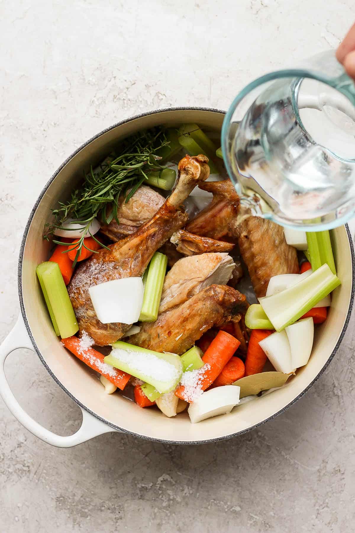 Turkey bones, celery, carrots, garlic, onion, herbs, and salt in the dutch oven with water being poured over the top. 