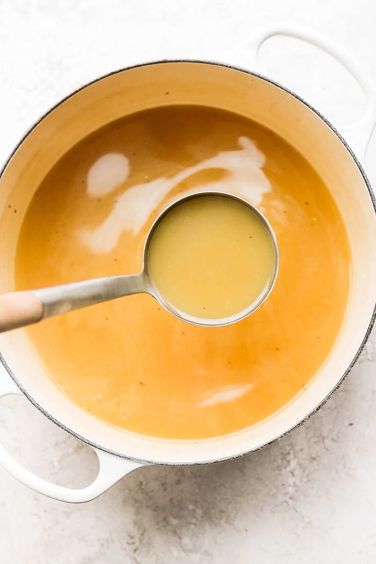 Turkey stock in a dutch oven being scooped out with a ladle. 