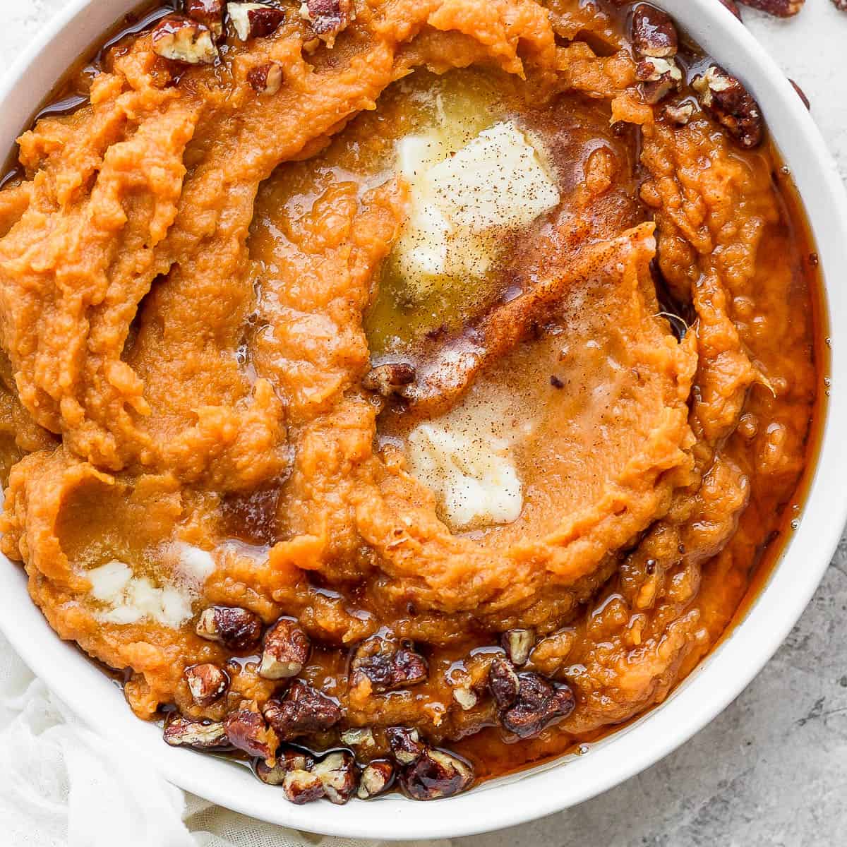 Bowl of mashed sweet potatoes with melted butter and candied pecans.