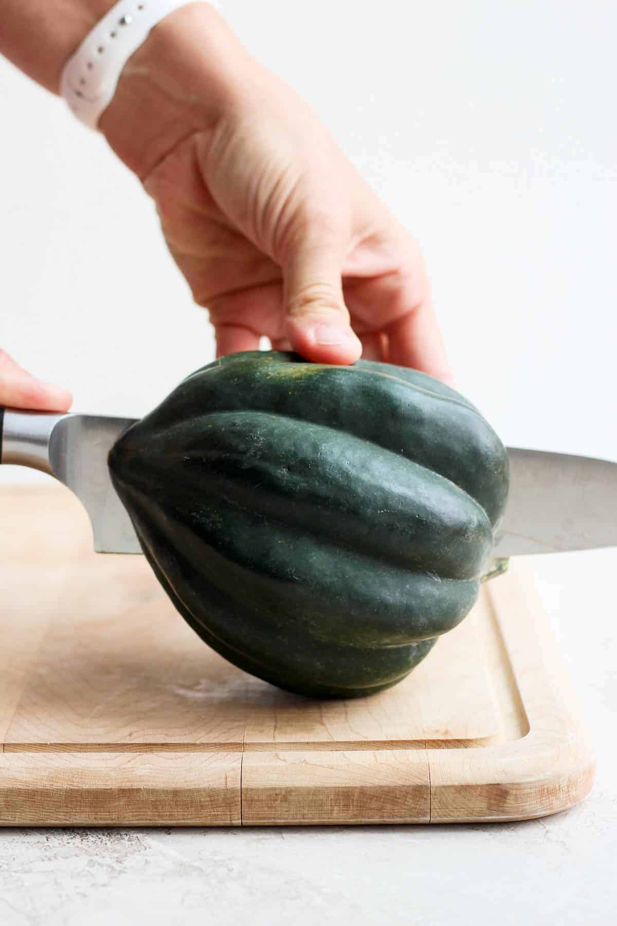 A hand cutting an acorn squash in half lengthwise using a knife for acorn squash soup.