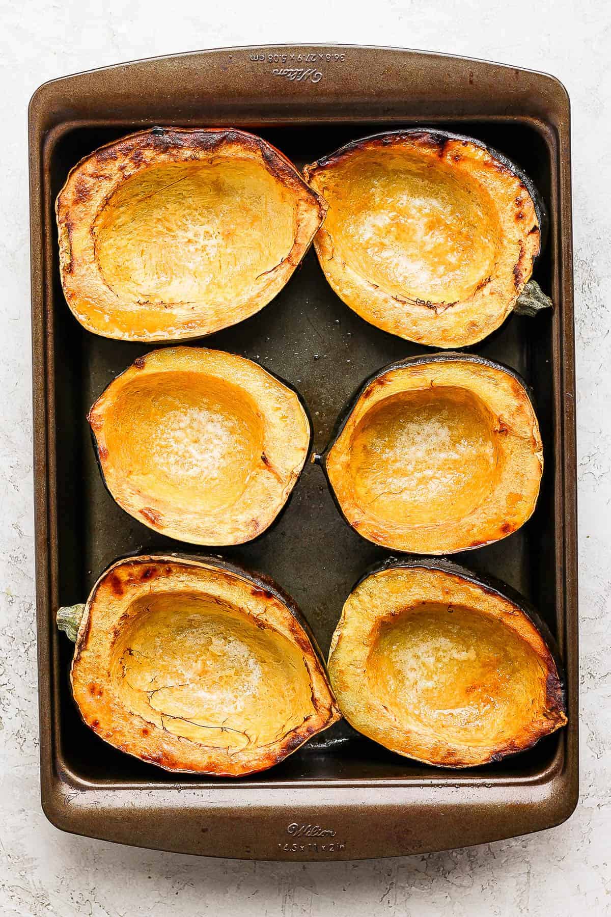 Three roasted halved acorn squashes in a baking dish to bake acorn squash soup.