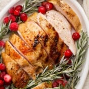 A platter with sliced smoked turkey breast on it along with cranberries and fresh rosemary.