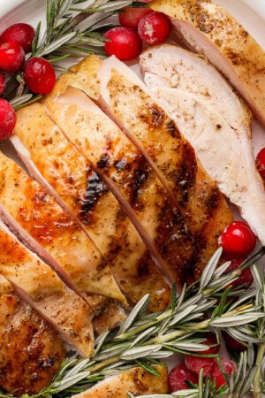 A platter with sliced smoked turkey breast on it along with cranberries and fresh rosemary.