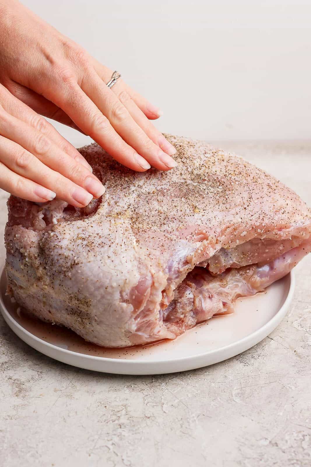 Someone rubbing a dry brine into a bone-in turkey breast on a plate.