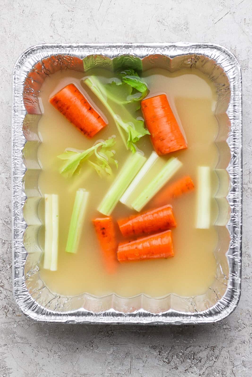 An aluminum pan with broth, carrots and celery inside.