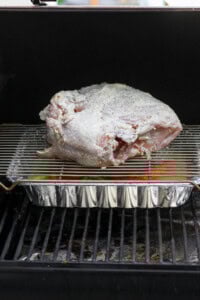 A raw bone-in turkey breast over a roasting pan on the smoker.