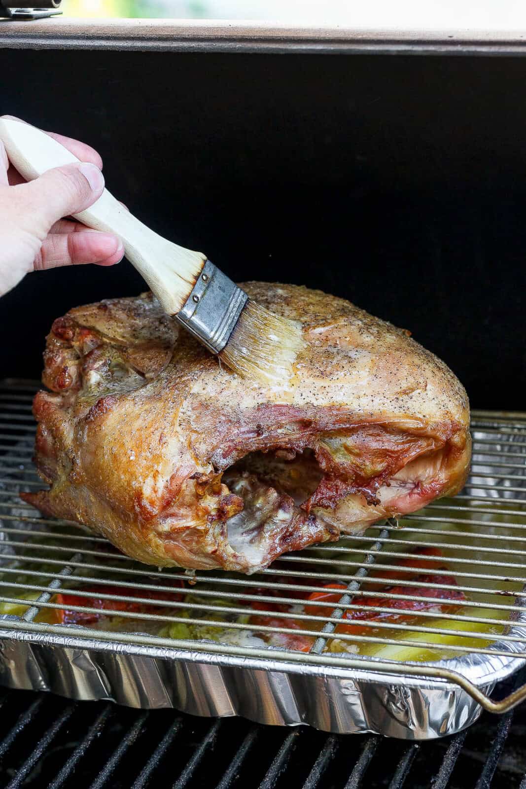A cooked smoked turkey breast being basted on the smoker.