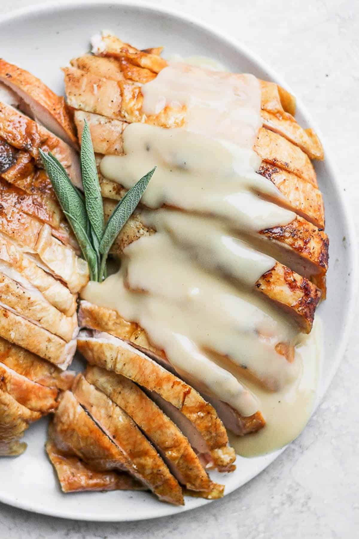 A sliced smoked turkey breast covered with gravy and garnished with sage leaves.