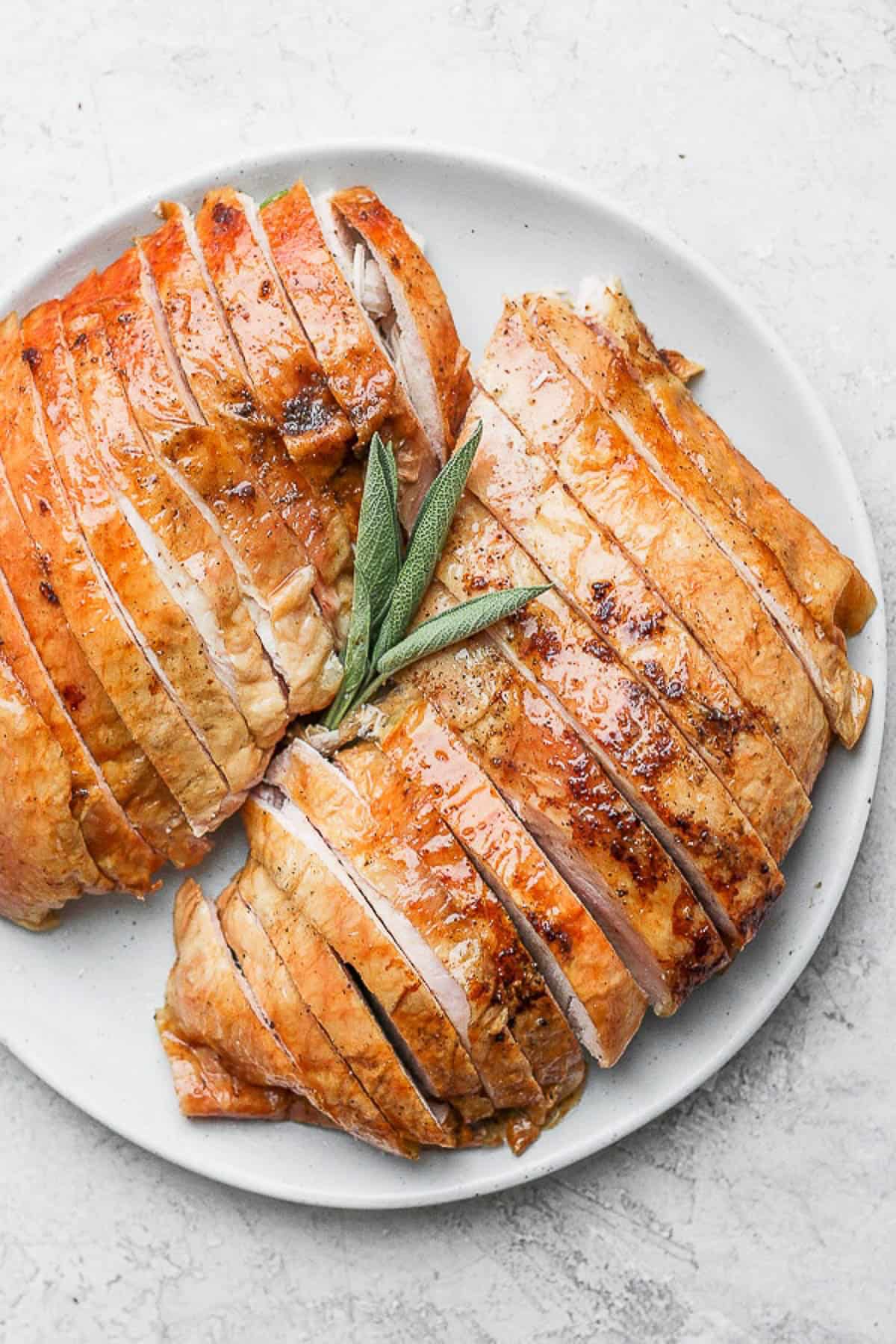 A sliced smoked turkey breast on a plate with sage leaves.