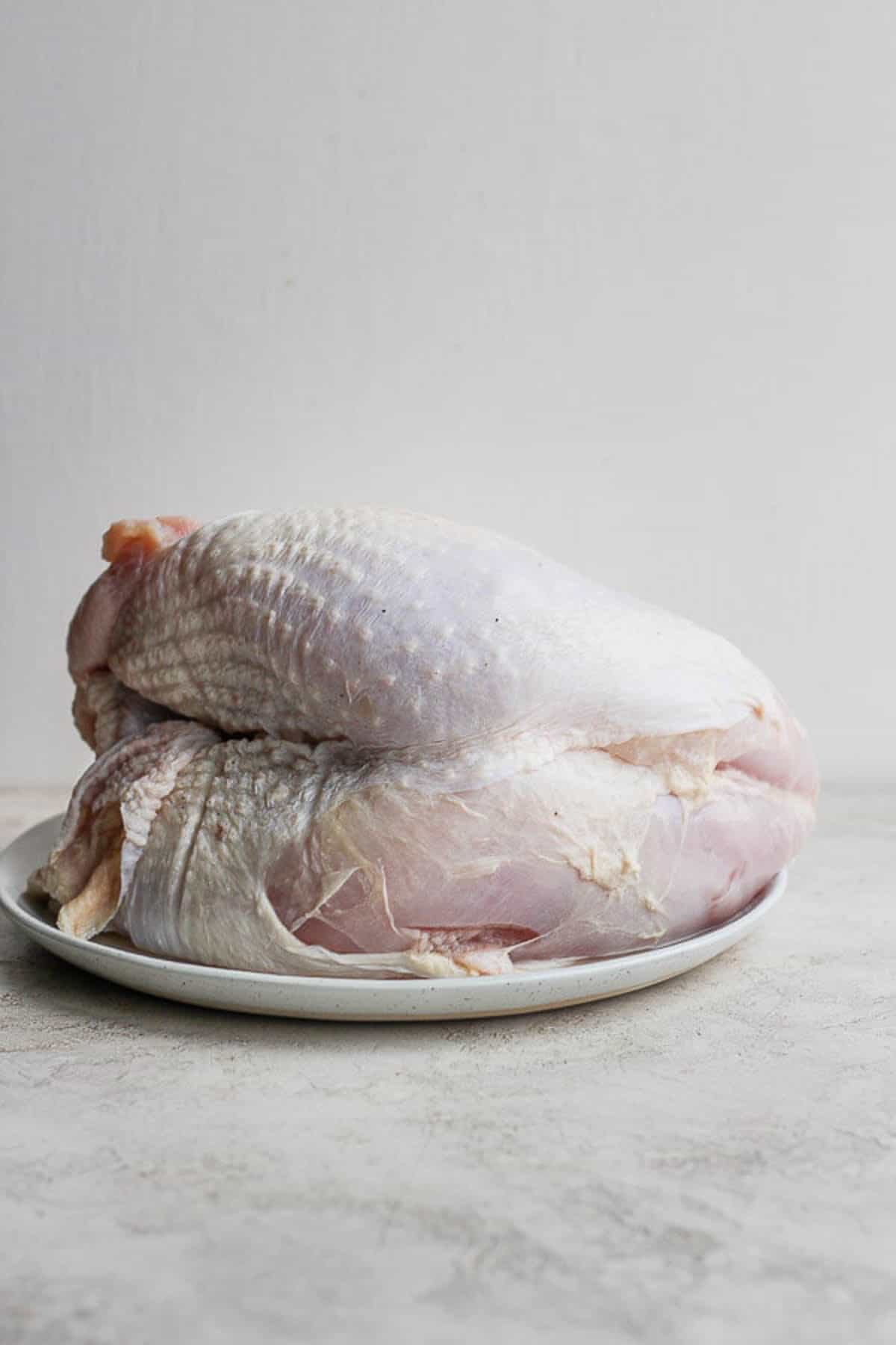 A raw bone-in turkey breast on a plate.