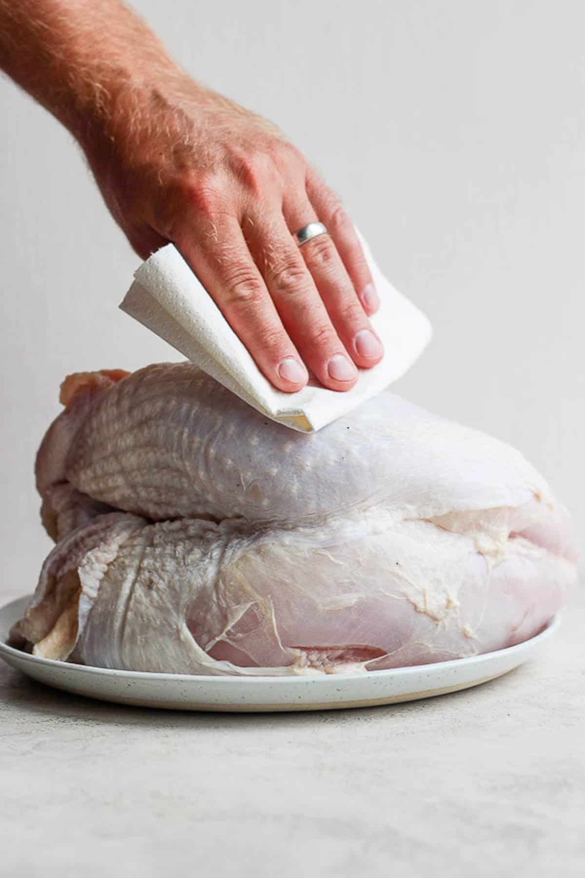 Someone patting a raw turkey breast dry with a paper towel.