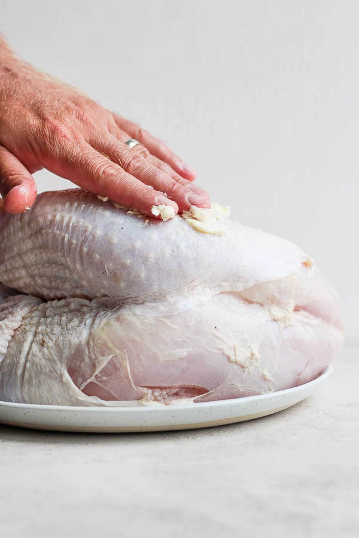 Someone rubbing softened butter on a raw turkey breast.