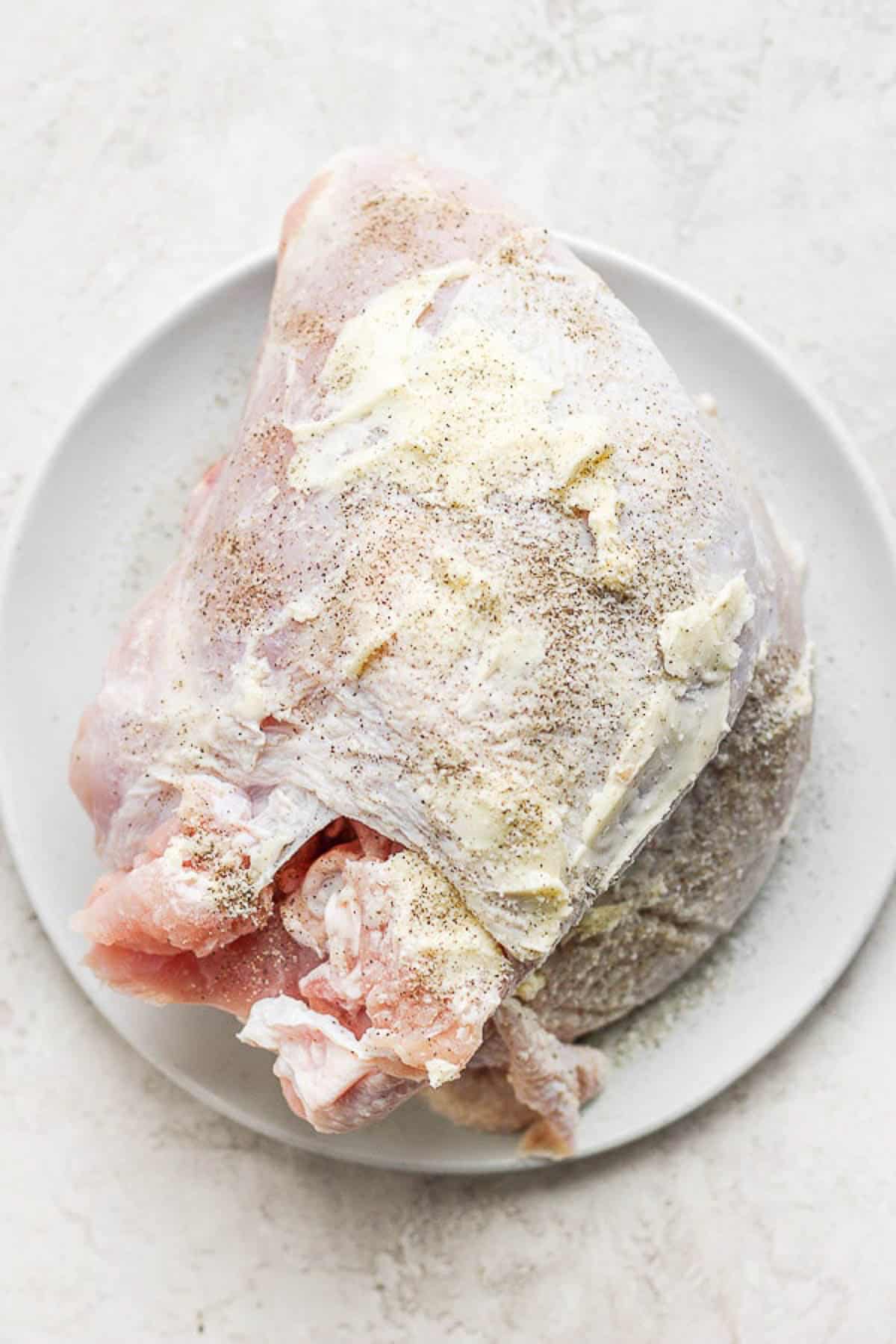 A turkey breast covered in softened butter and seasoning and ready for the smoker.