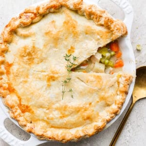 A turkey pot pie in a pie pan with a slice taken out and golden spoon next to it.