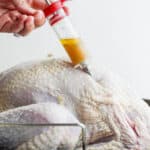 Someone injecting a turkey injection recipe into a raw turkey.