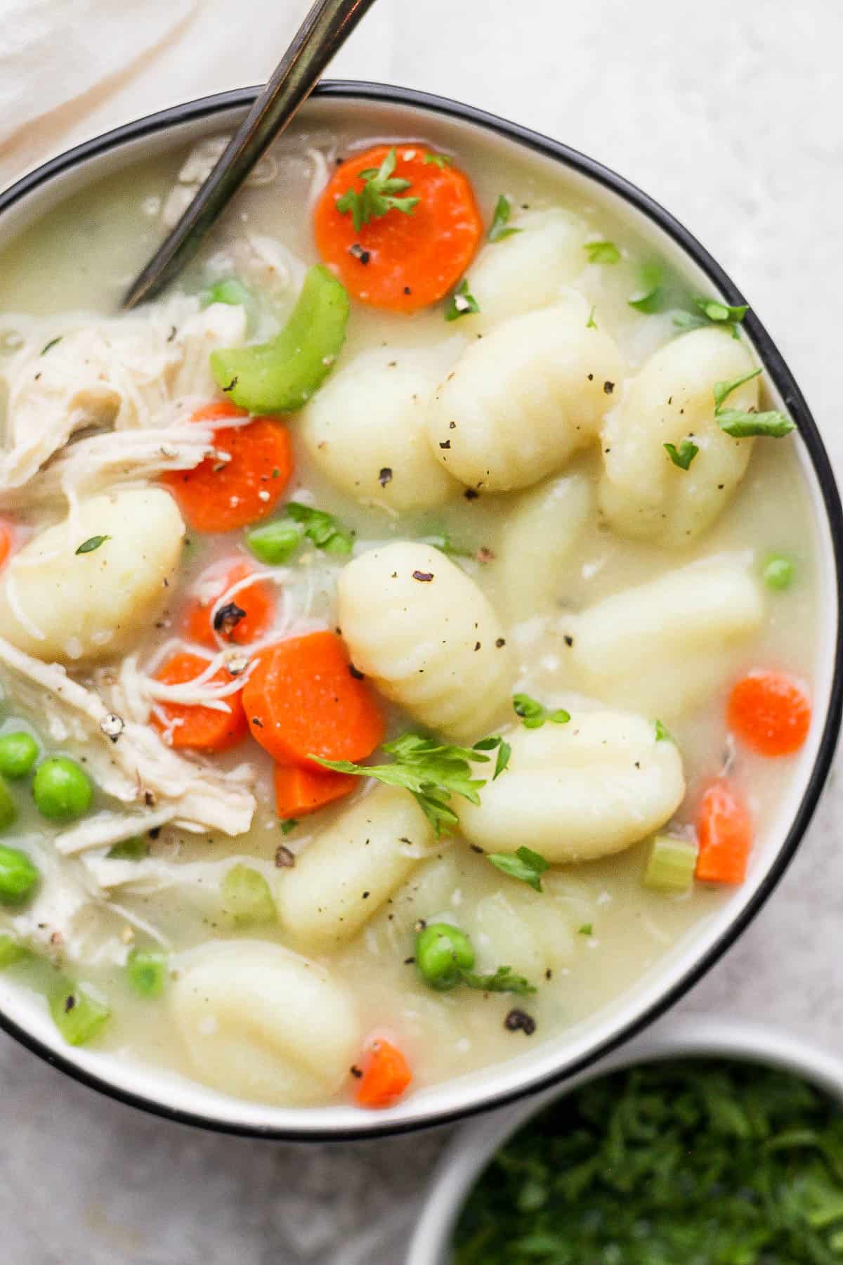 Chicken gnocchi soup in a bowl topped with fresh herbs.