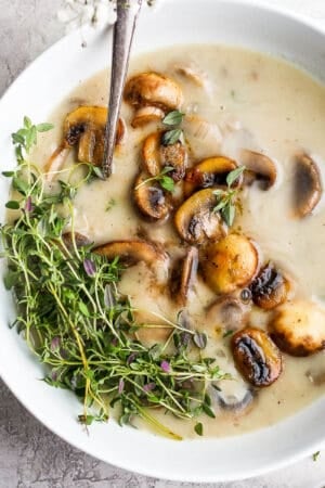 Bowl of dairy free cream of mushroom soup with sauteed mushrooms and fresh thyme on top.