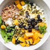 A bowl of fall farro salad with farro, arugula, delicata squash and goat cheese.