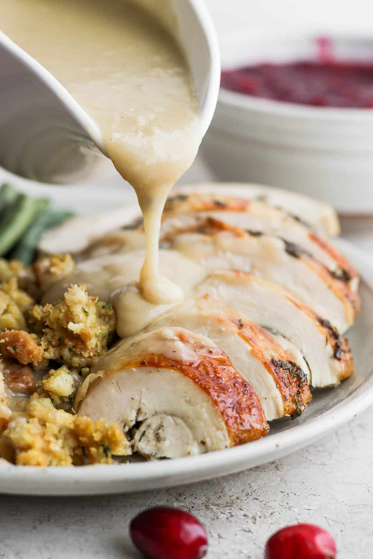 Someone pouring giblet gravy over sliced turkey breast on a plate next to stuffing.