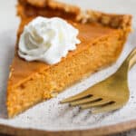 A slice of gluten free pumpkin pie on a plate with a fork and whipped cream on top.