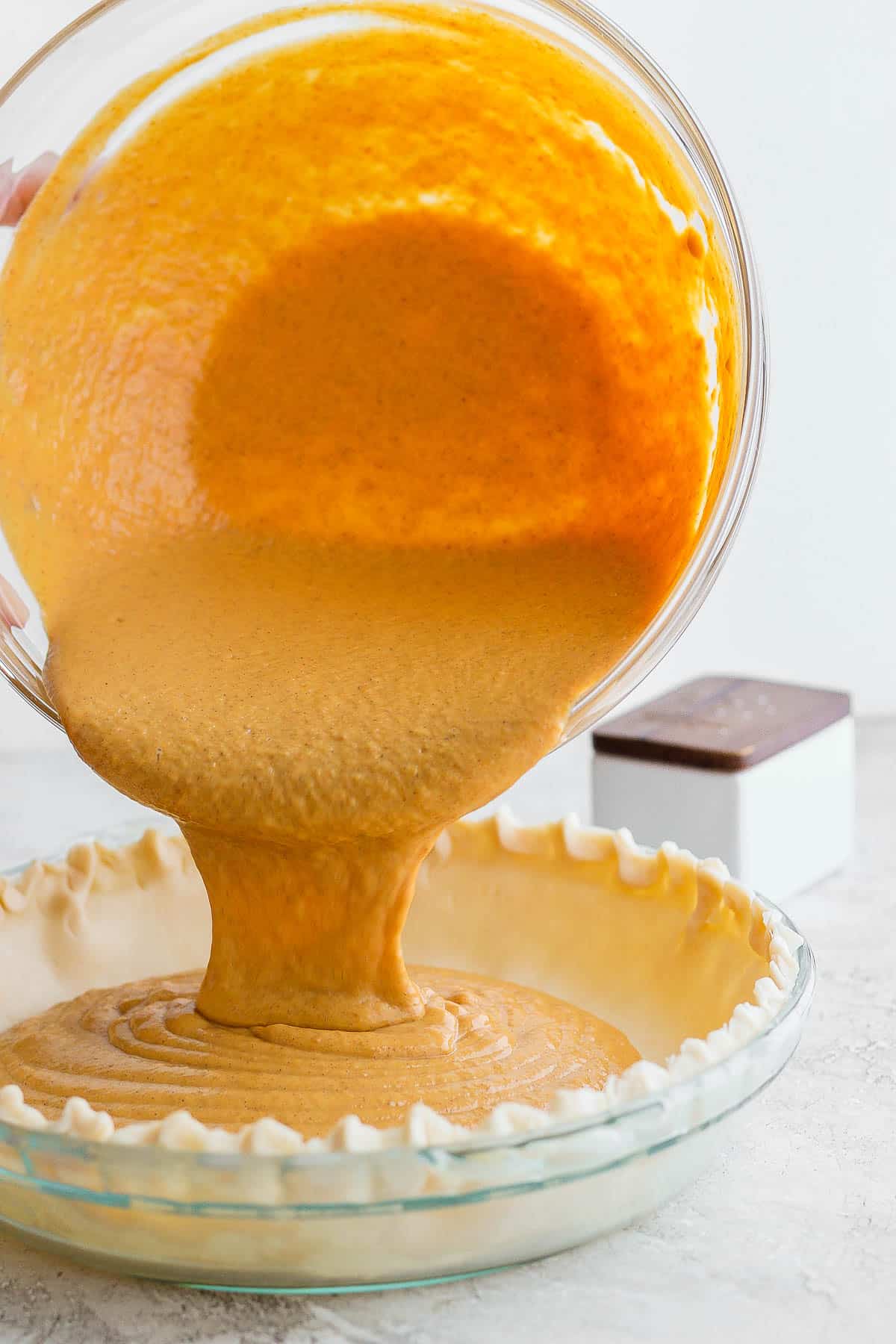 The fully mixed pumpkin pie filling being poured into a pie pan lined with the gluten free pie crust.
