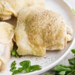 A boiled chicken thigh on a plate with salt and pepper and parsley garnish.