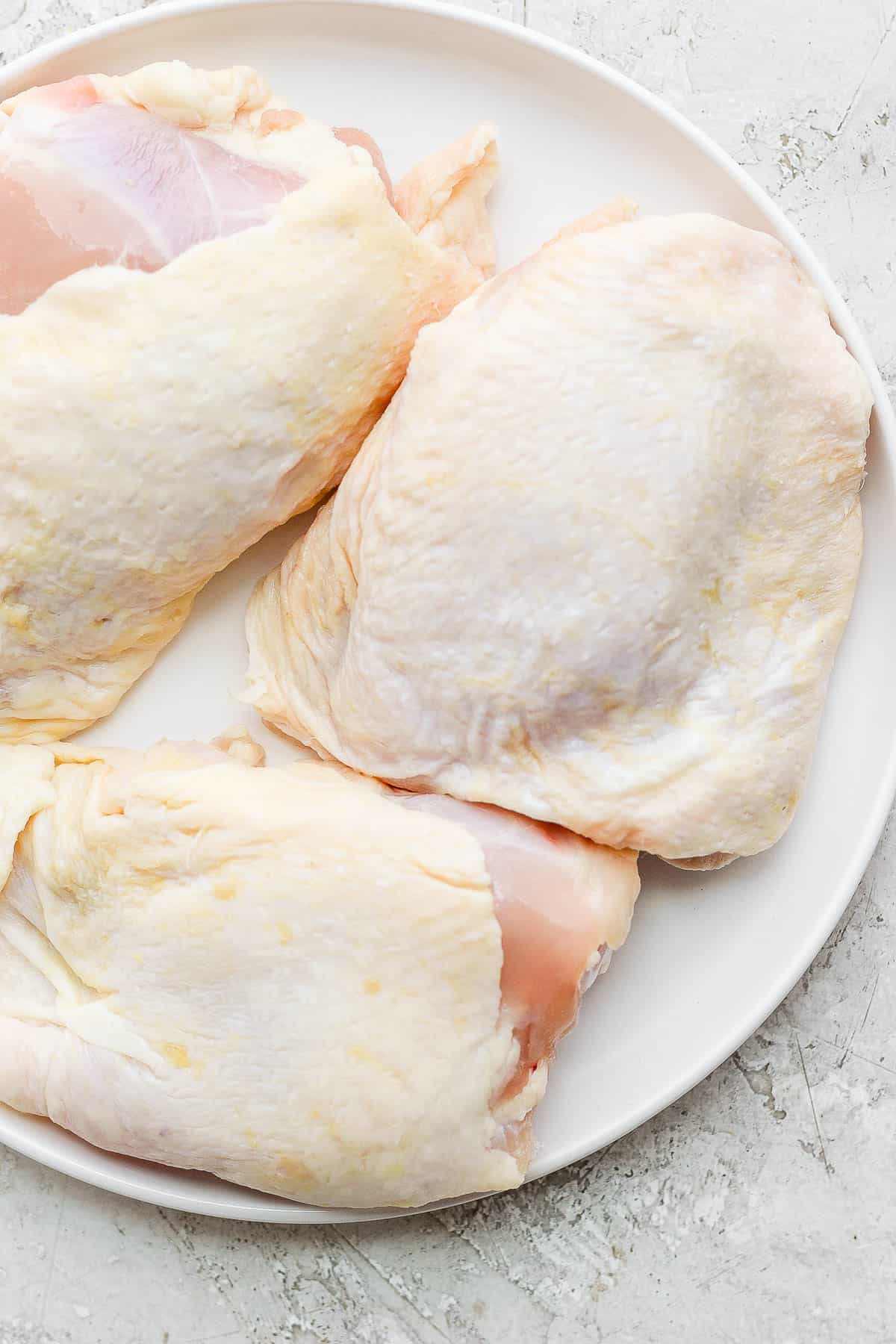 Three bone-in, skin-on chicken thighs on a white plate.