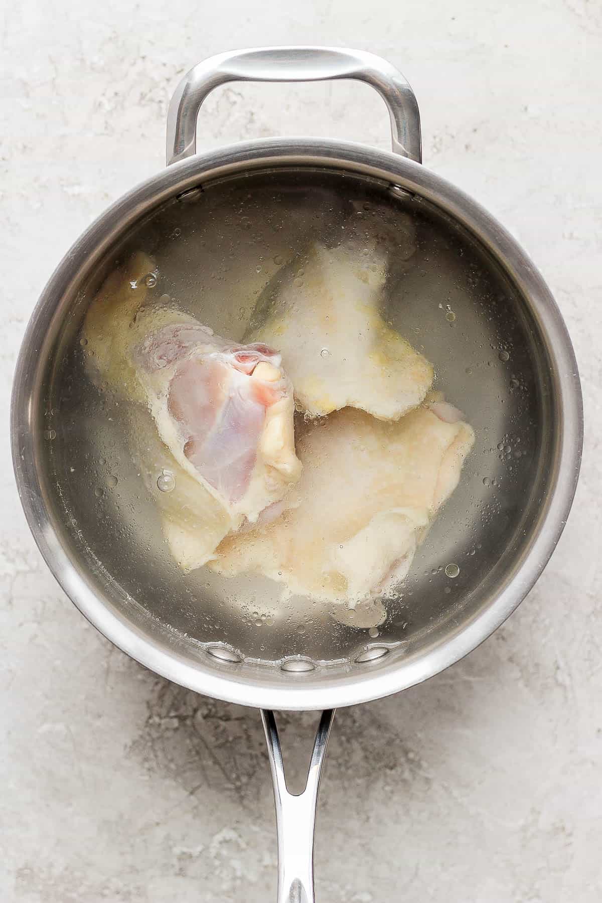 Three chicken thighs in a pot of water.