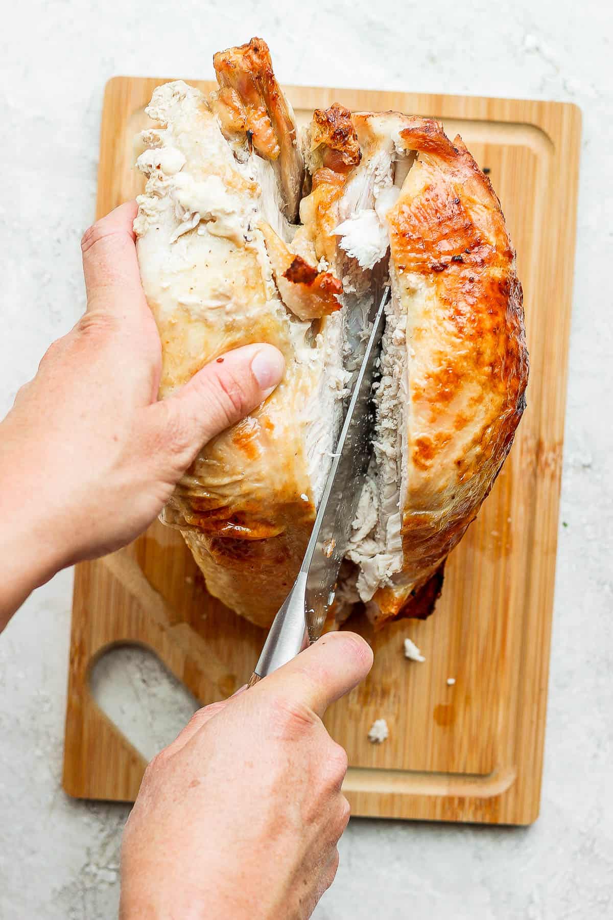 A knife slicing down the breastbone to remove the turkey breast from one side.