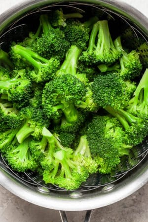 Steamed broccoli in a saucepan with a steamer basket inside.