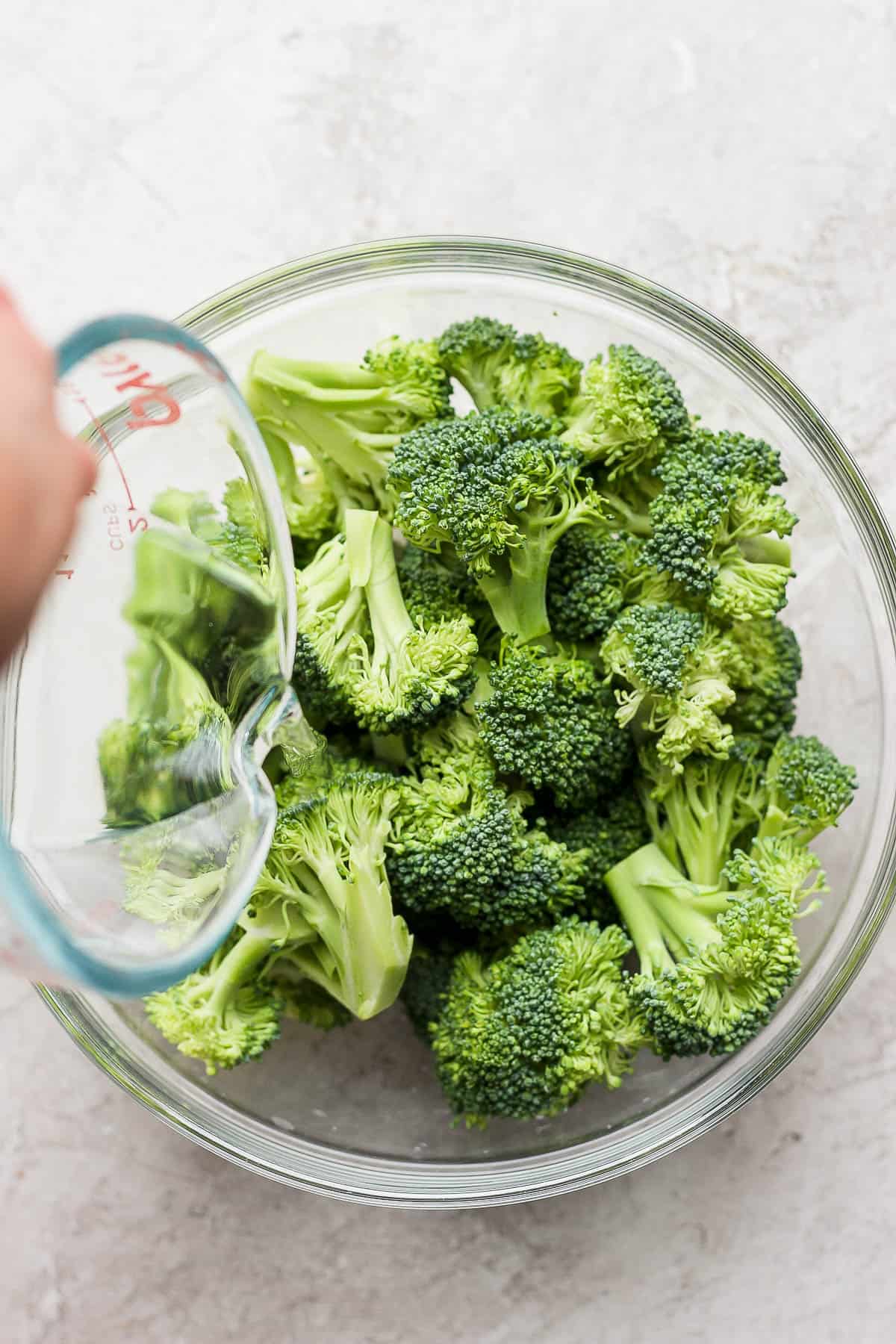 Water being poured into a microwave safe bowl with broccoli in it.