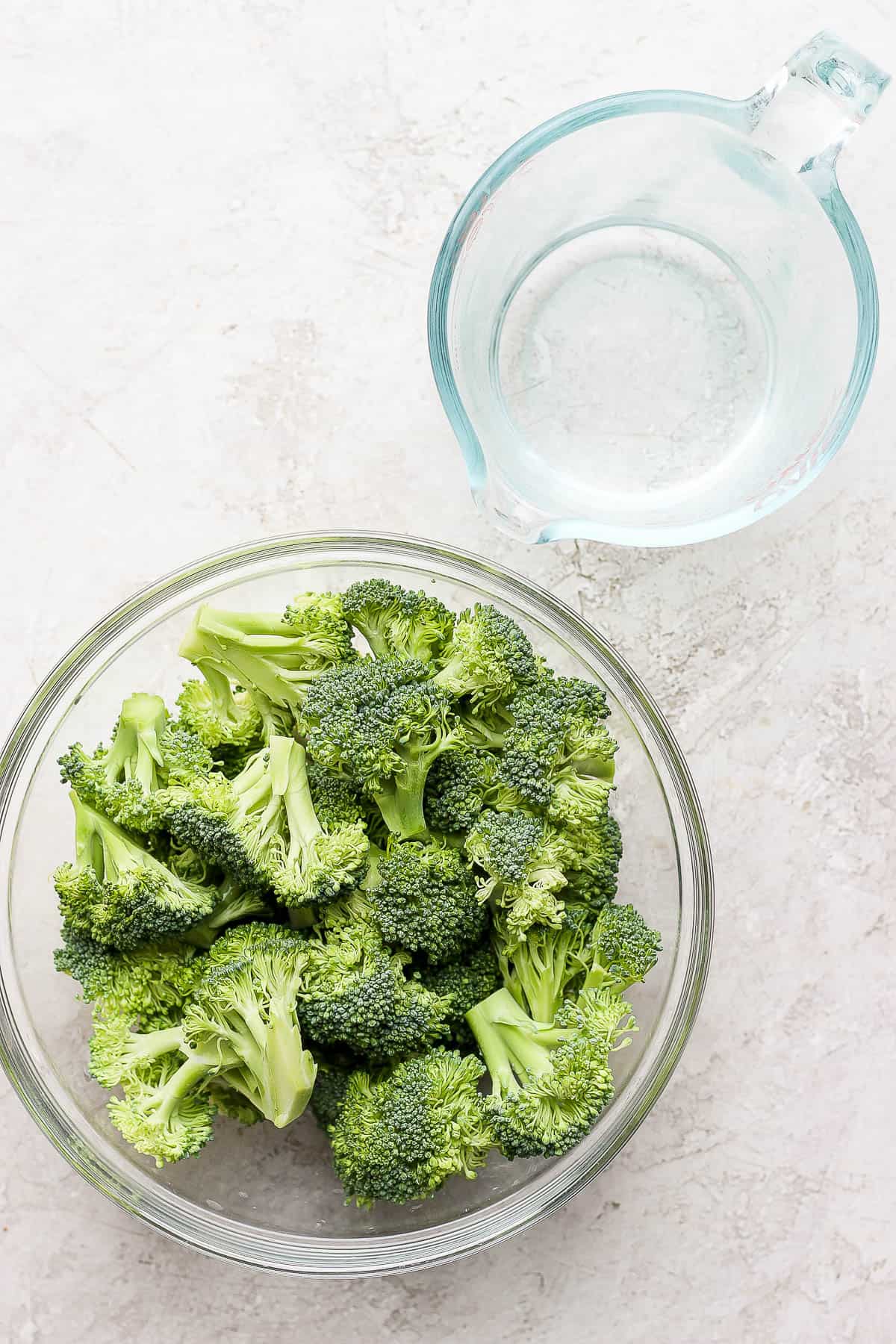 Broccoli in a bowl and a measuring cup with water.