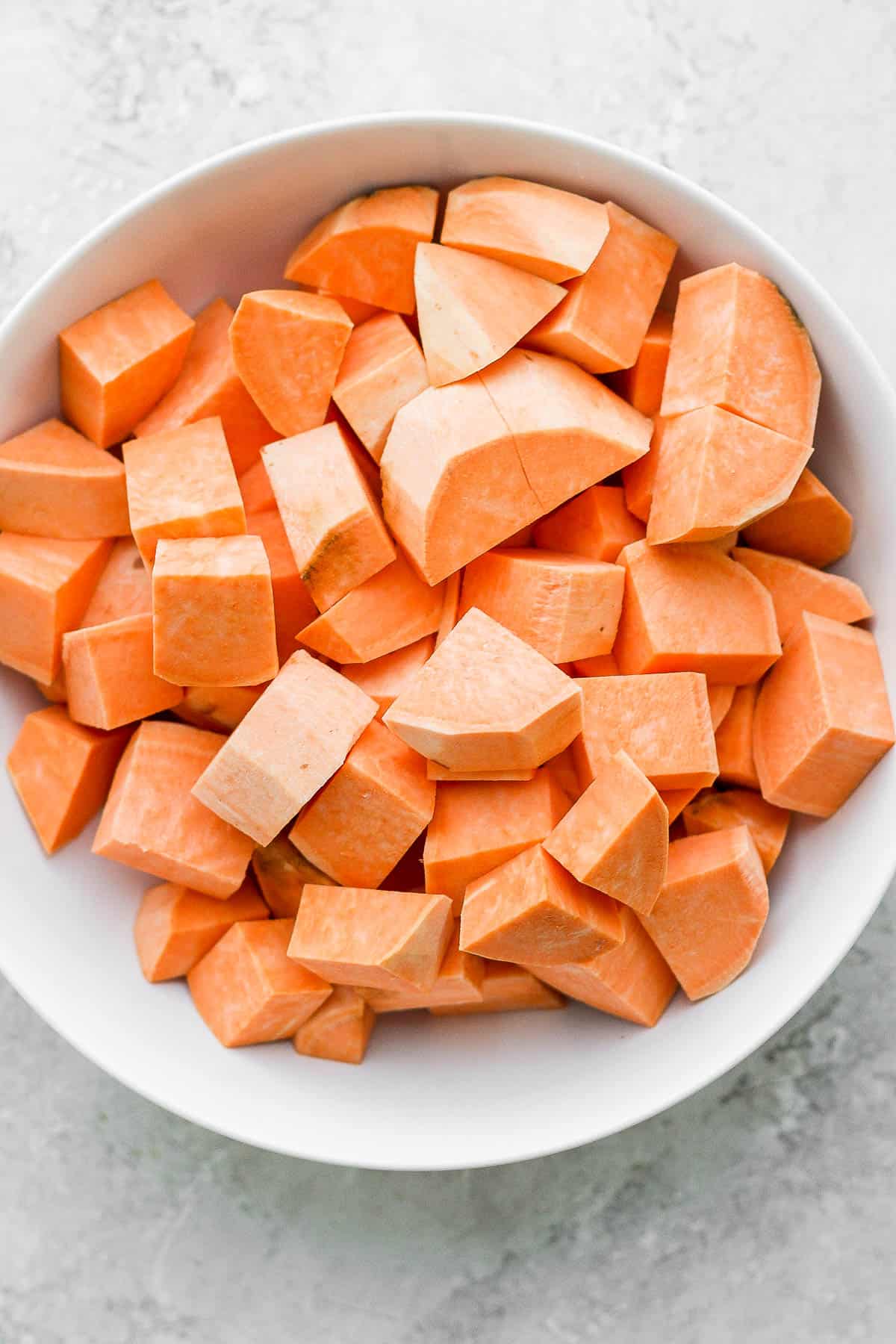Peeled and cubed sweet potatoes in a white bowl.