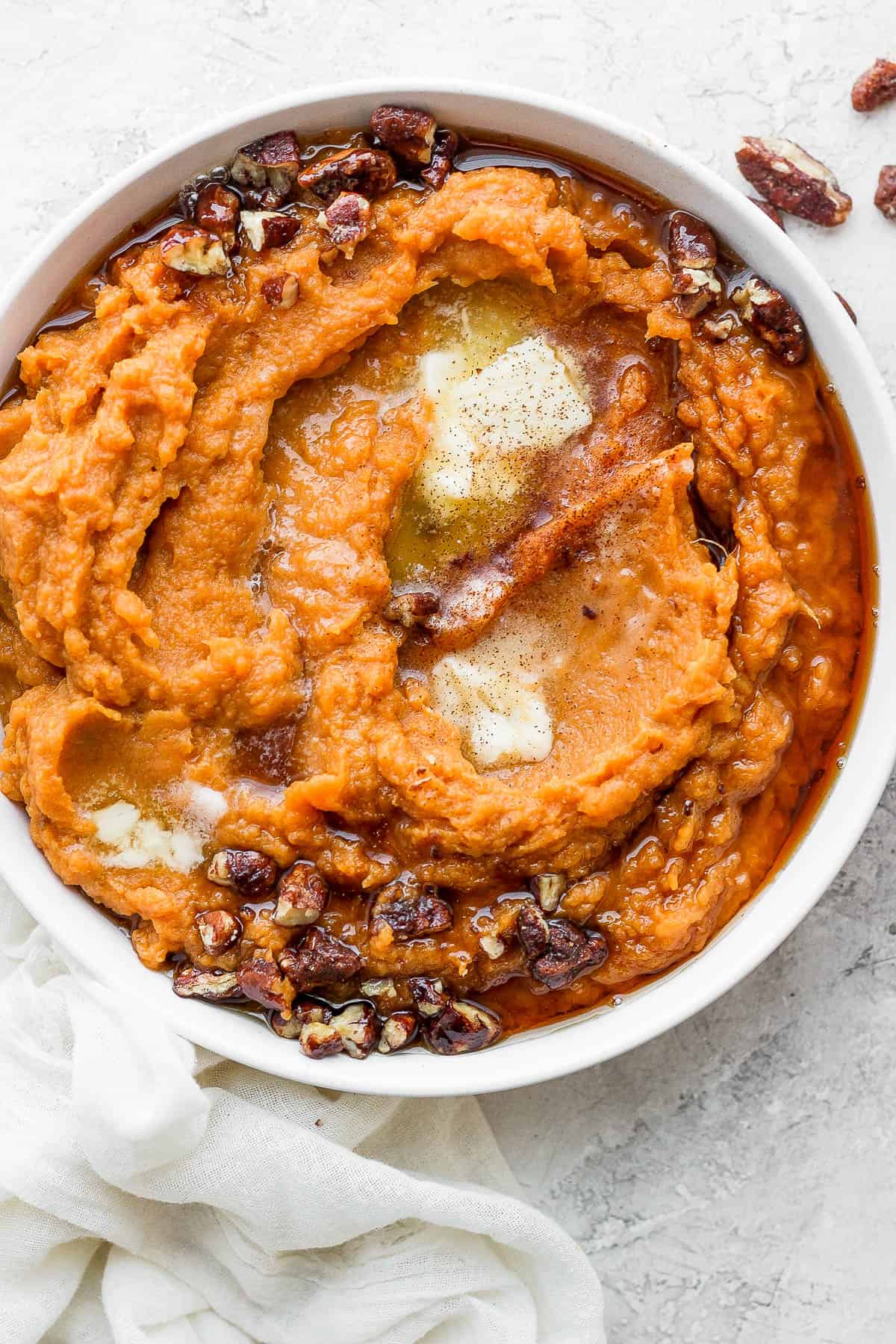 Completed mashed sweet potatoes in a bowl topped with butter, maple syrup, and pecans. 