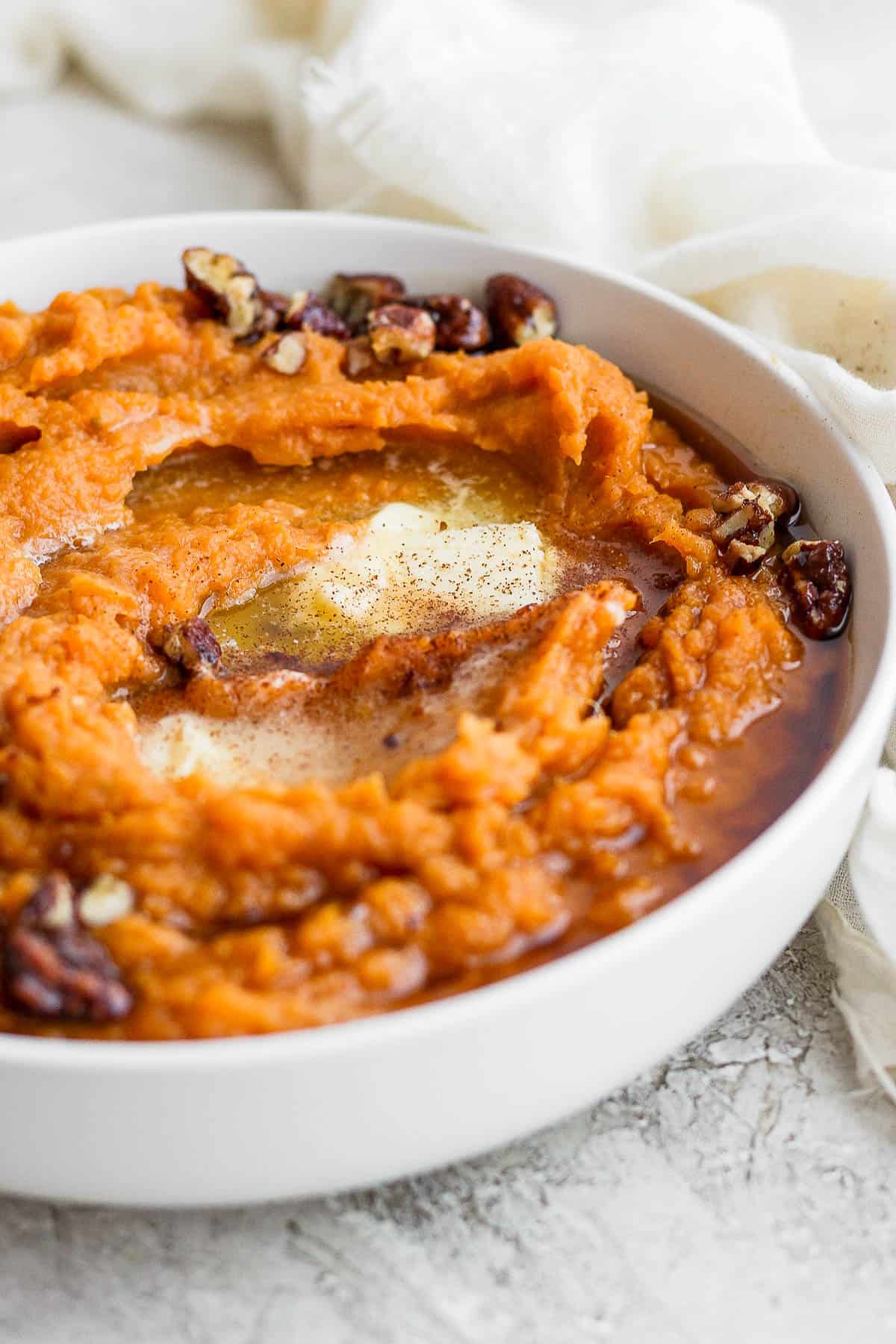 Completed mashed sweet potatoes in a bowl topped with butter, syrup, and pecans. 