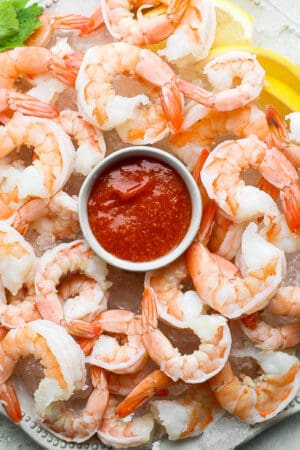 A plate of shrimp cocktail on ice with a bowl of cocktail sauce in the center.