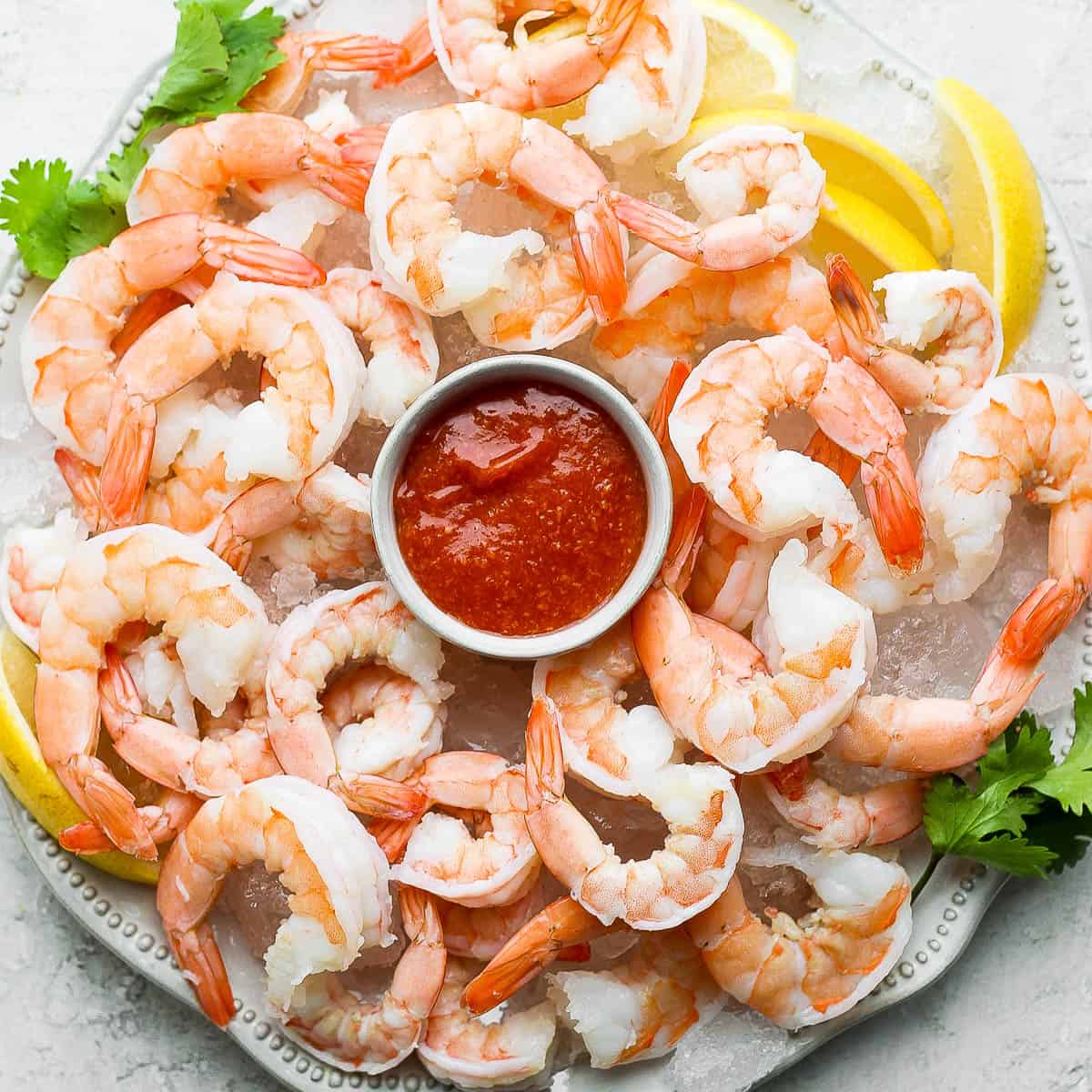 A plate of shrimp cocktail on ice with a bowl of cocktail sauce in the center.