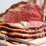 A smoked prime rib on a cutting board, sliced, with herbed butter.