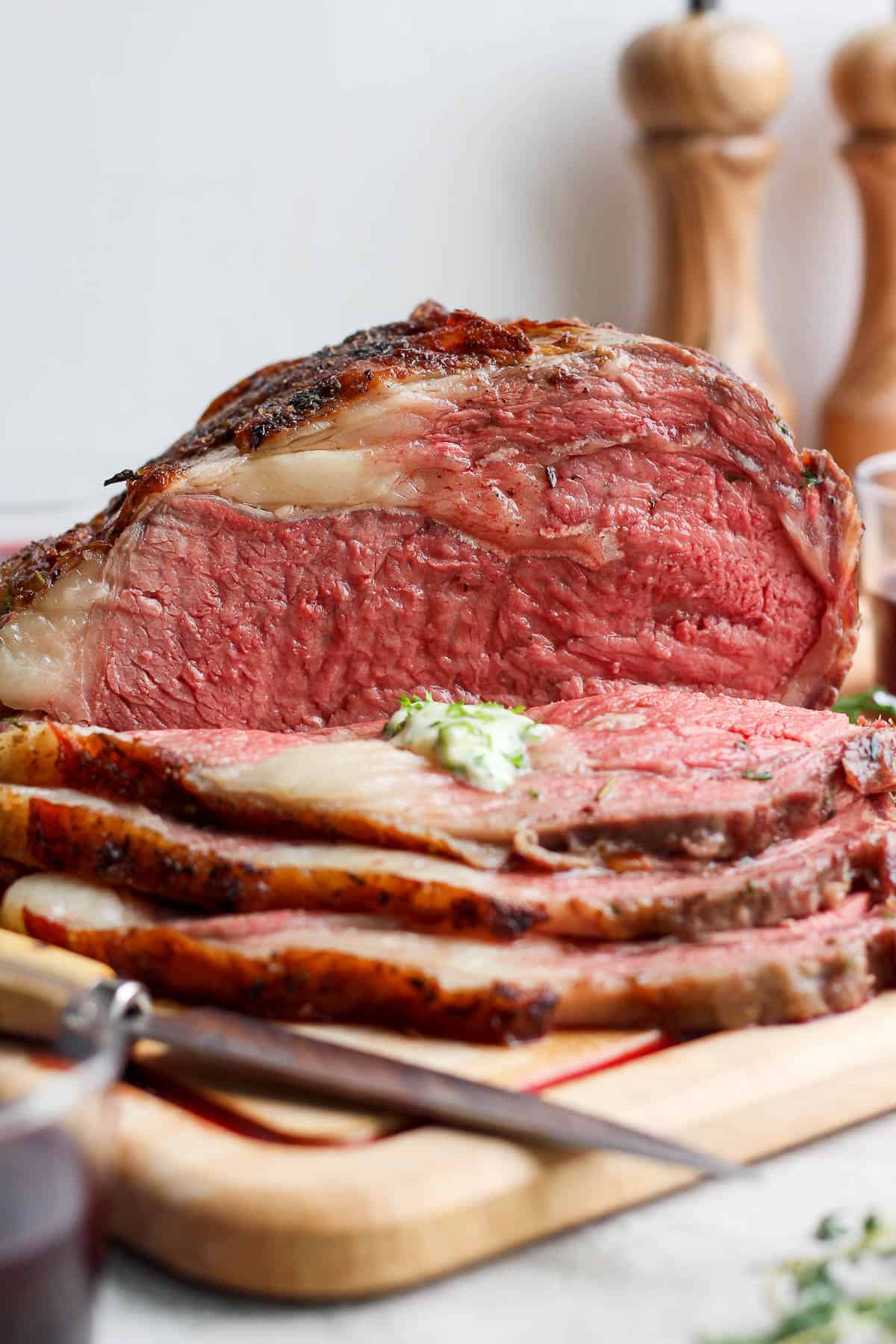 A fully cooked prime rib on a cutting board. Half of the prime rib is sliced and the other half is whole.