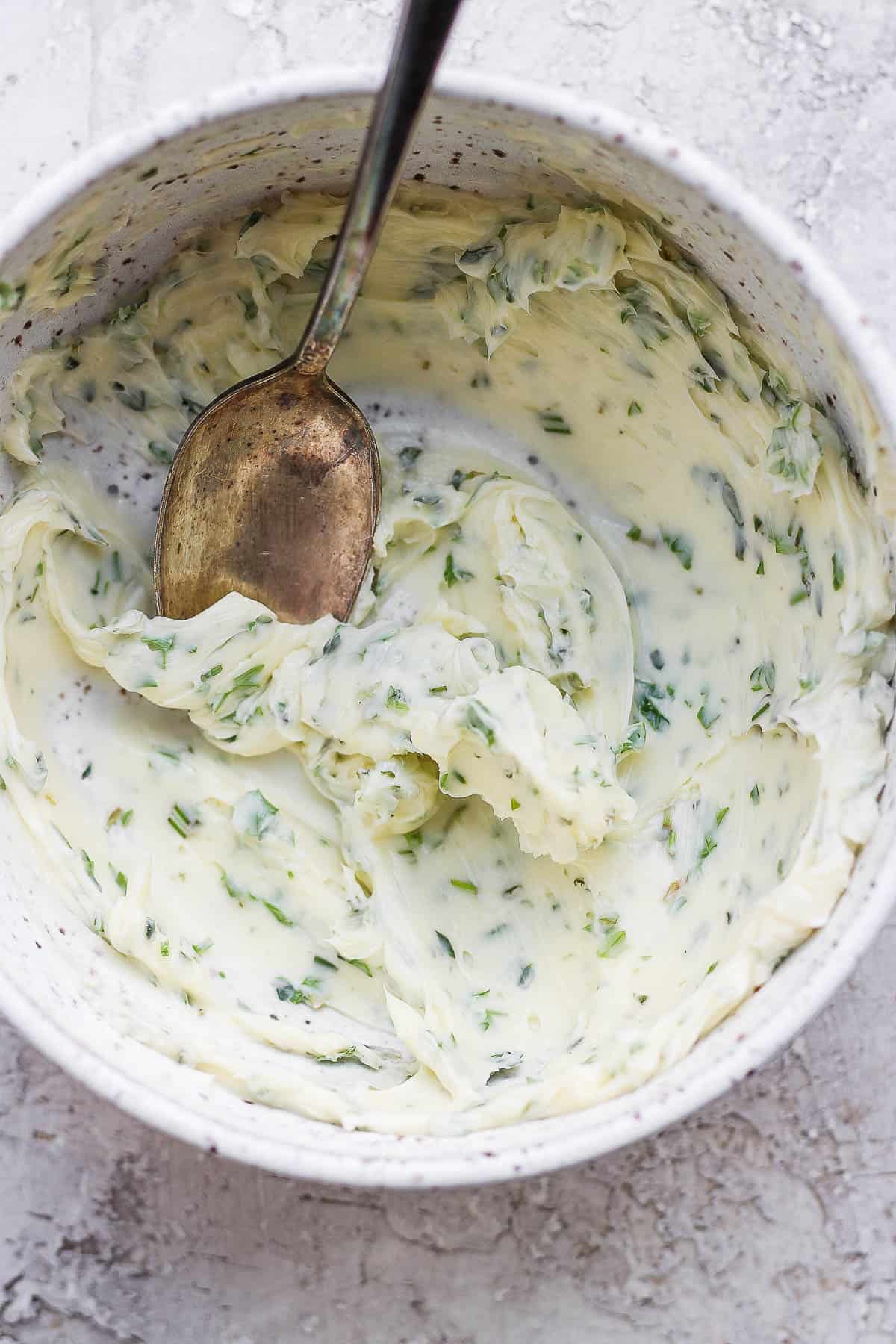 A bowl of herbed butter in a bowl with a spoon.