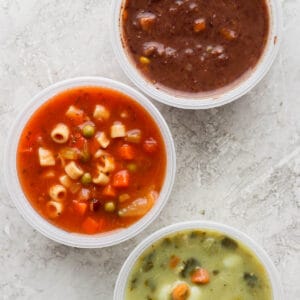 Top shot of three plastic containers with three different soups in them.