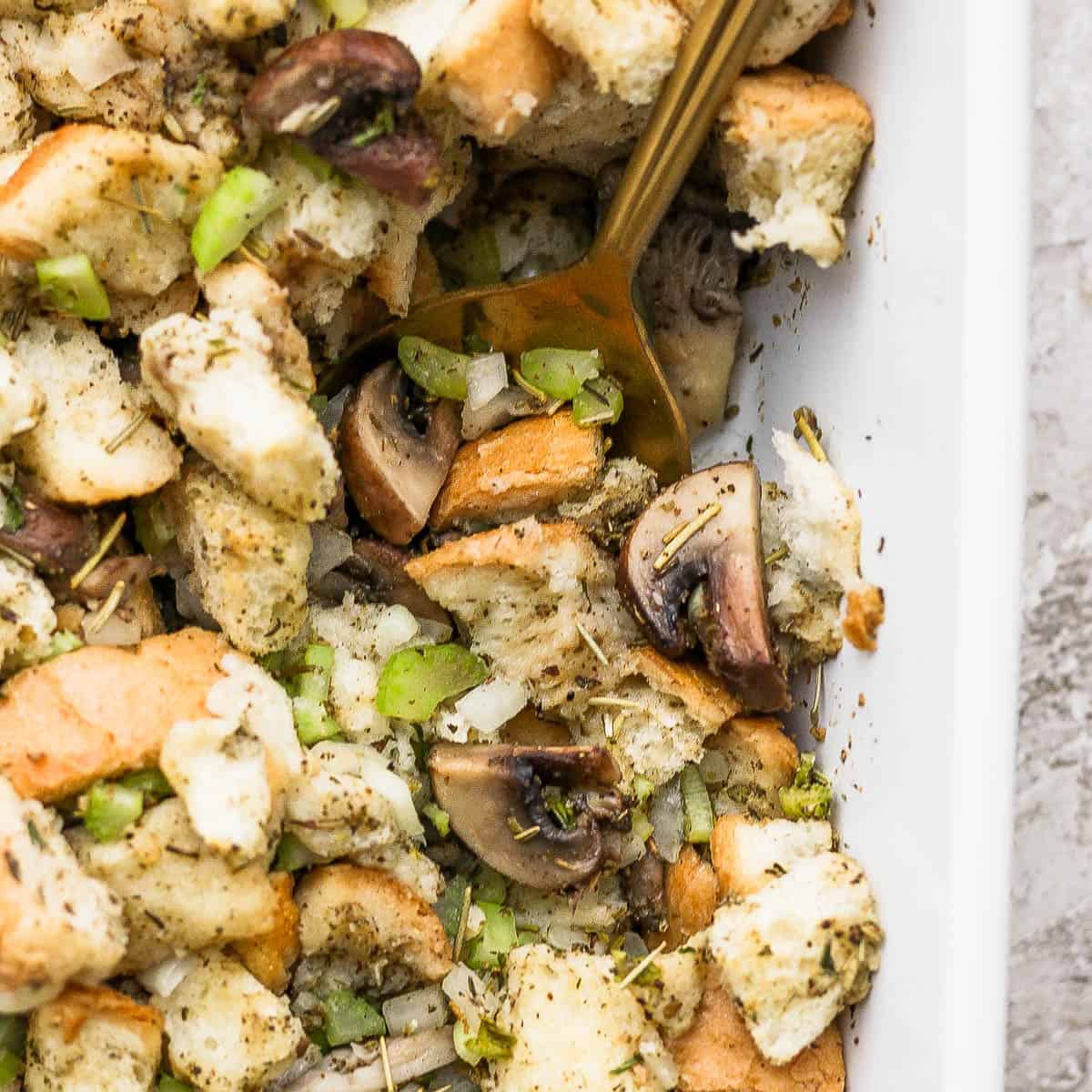 Close up of sourdough stuffing in a baking dish with a golden spoon.