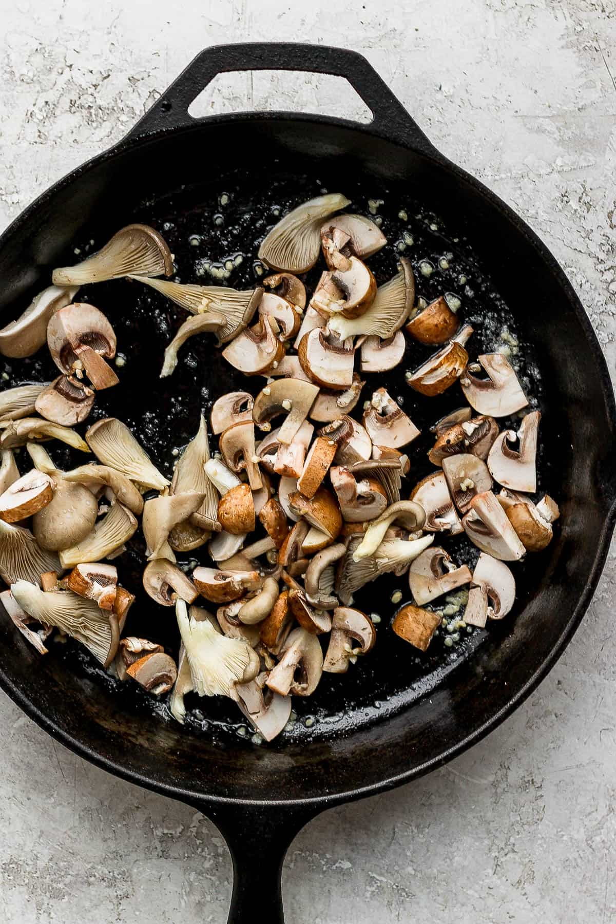 The garlic and mushrooms sautéing in a cast iron pan.