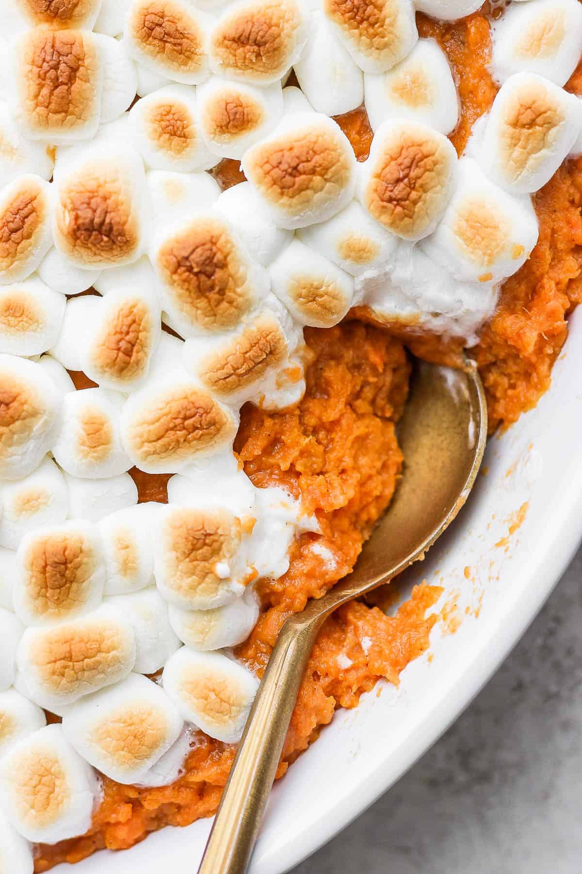 A close up of the sweet potato casserole with marshmallows with a spoon inserted into the side.