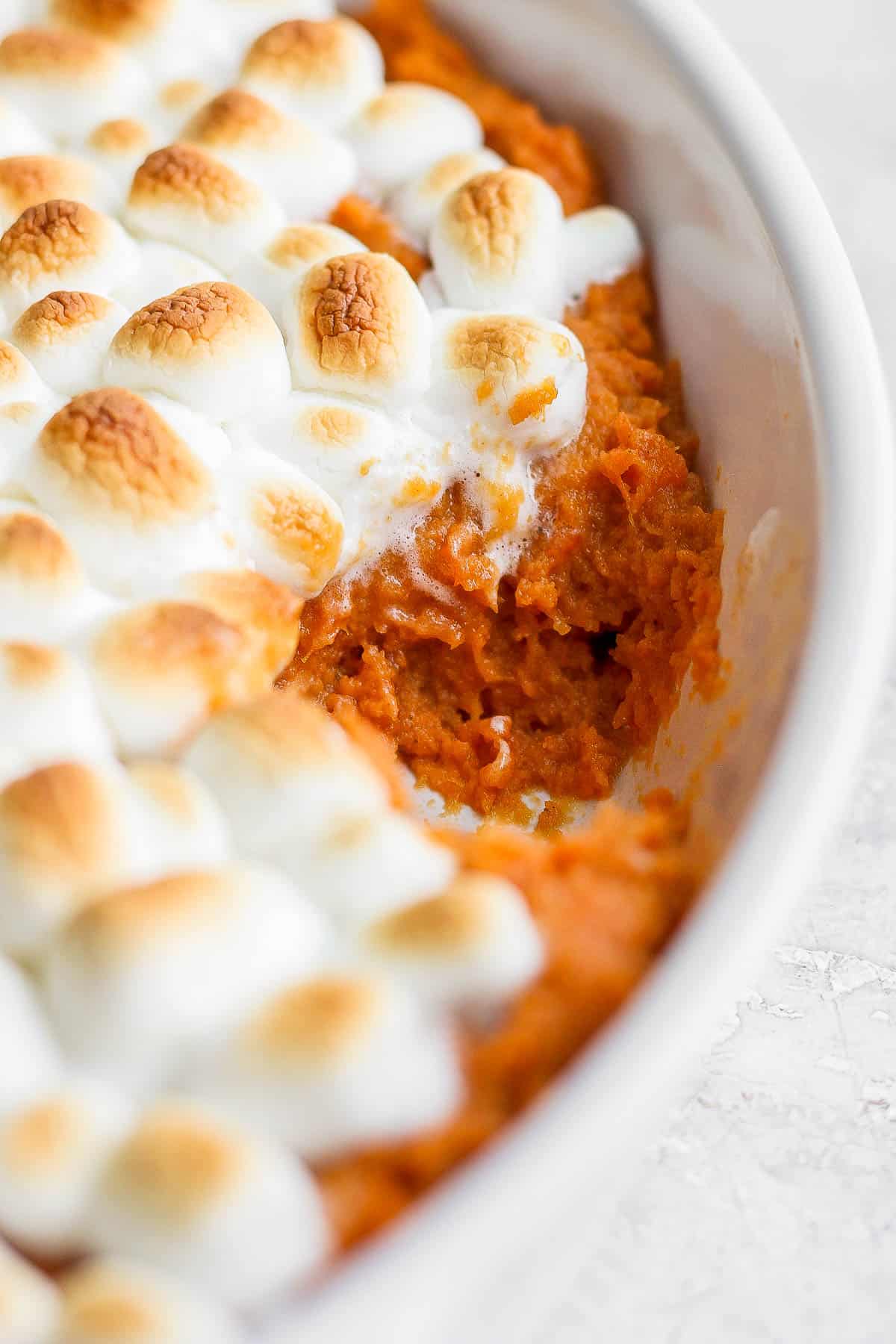 Sweet potato casserole with marshmallows in a casserole dish with a section removed in order to see the creamy middle.