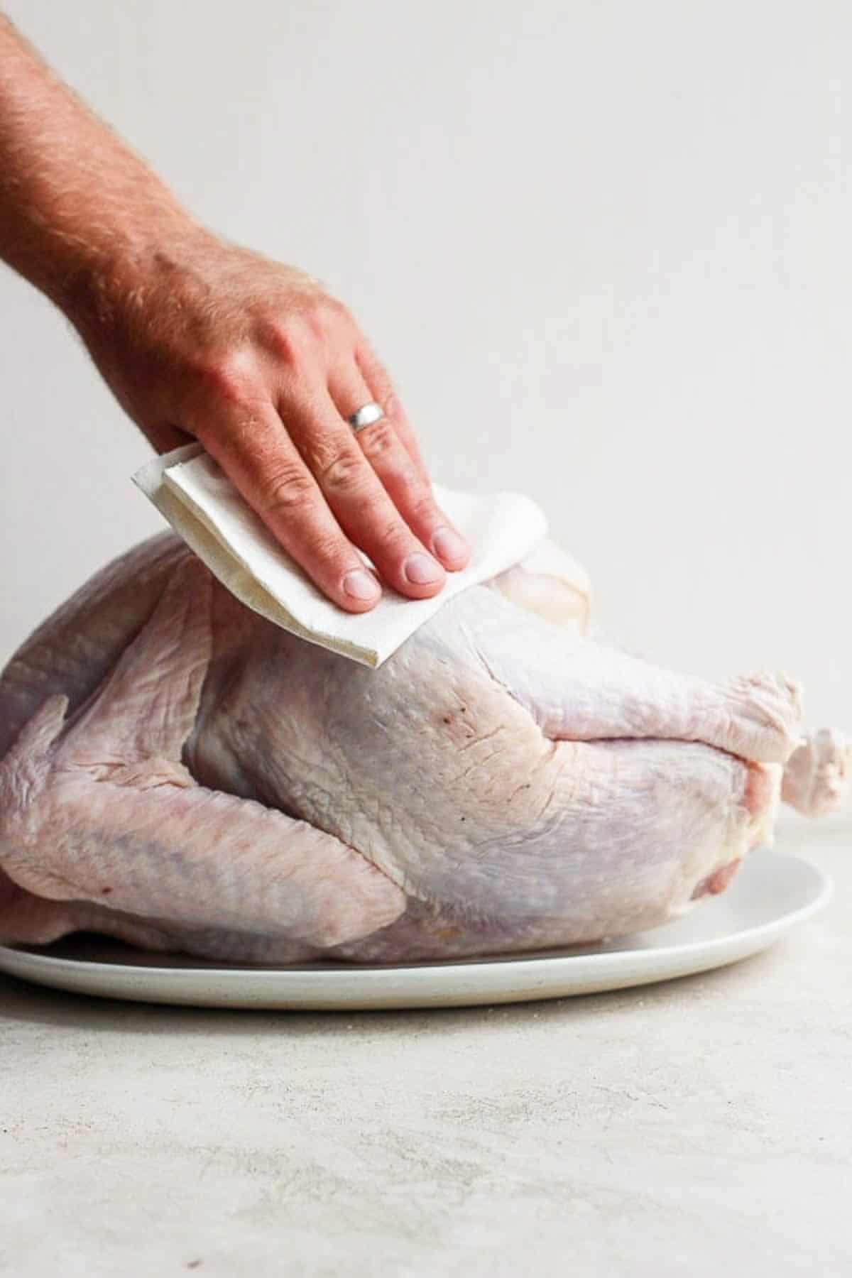 Someone patting a whole turkey dry with a paper towel.