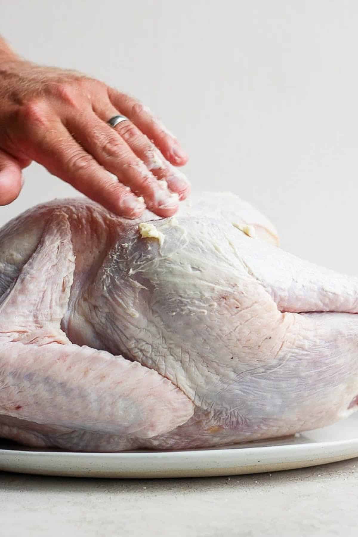 Someone rubbing softened butter on a whole turkey.