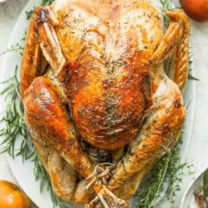 Top shot of a fully cooked thanksgiving turkey on a platter with herbs around it.