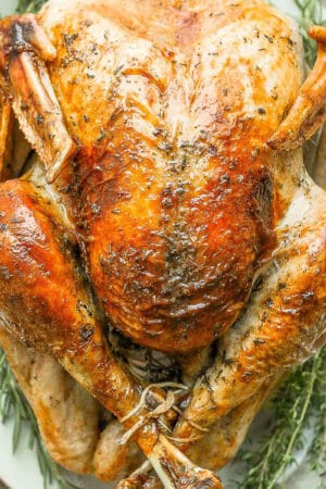 Top shot of a fully cooked thanksgiving turkey on a platter with herbs around it.
